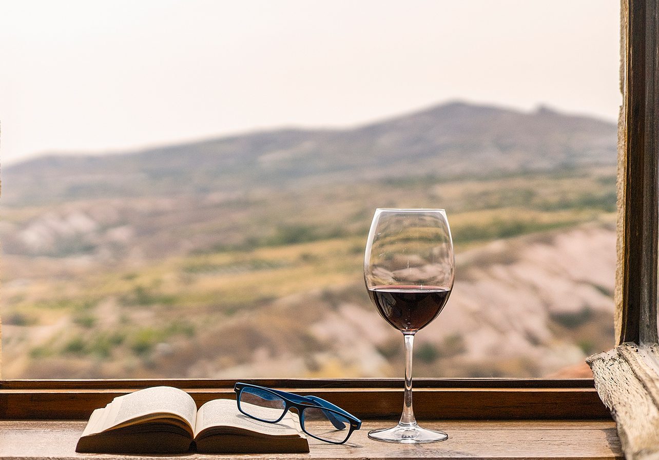Wine glass, book, and glasses by window.